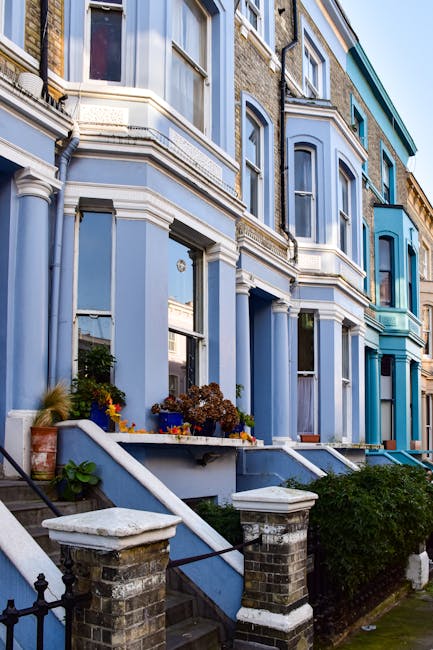 The image depicts the exterior of a multi-story residential building with a predominantly blue facade, featuring bay windows and decorative architectural elements. The building's surfaces include smoo
