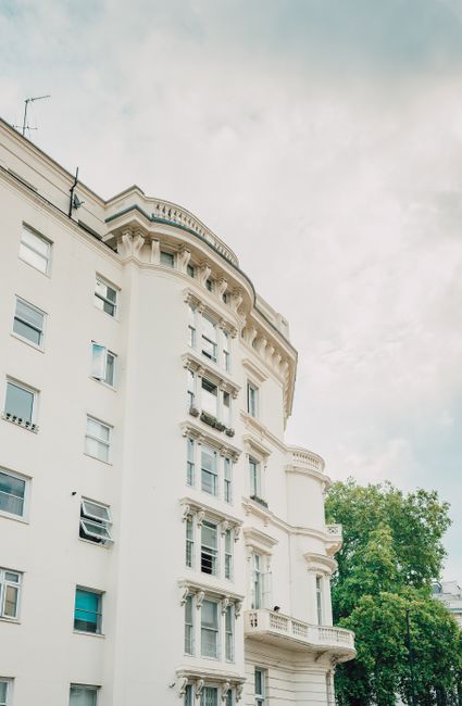 The image depicts the exterior of a multi-story residential building with a predominantly blue facade, featuring bay windows and decorative architectural elements. The building's surfaces include smoo